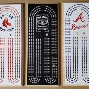 May include: Three wooden game boards with different team logos and names. The first board has a red and white Boston Red Sox logo. The second board has a black and white Jack Daniels logo. The third board has a blue and white Atlanta Braves logo.