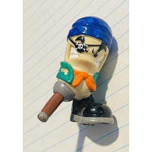 May include: A novelty toy figure of a pirate with a blue bandana, black eye patch with a skull and crossbones, and a green and orange vest. The figure has a brown handle and a black boot.