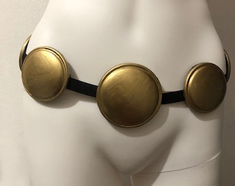 May include: A gold-colored belt with four round, decorative pieces. The belt is made of black leather and has a simple design.