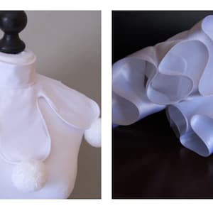 May include: White ruffled collar with pom-poms on the edges. The collar is made of a soft, white fabric and is designed to be worn as a costume accessory.