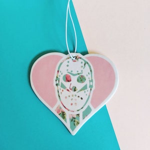 May include: A pink heart-shaped car air freshener with a white floral pattern and a white hockey mask with a floral pattern.