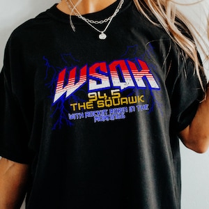 May include: Black t-shirt with the text "WSQK 94.5 The Squawk with Rockie Rizin in the Mornings" in red, white, and blue. The graphic has a retro design with lightning bolt accents. The shirt has short sleeves and a crew neck.