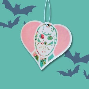 May include: A pink heart-shaped car air freshener with a white floral pattern and a white hockey mask with a floral pattern.