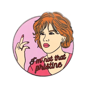 Puede incluir: Un pin de esmalte rosa y rojo con una mujer de dibujos animados de pelo rojo haciendo el dedo medio. El texto "I'm not that pristine" est&aacute; escrito en cursiva roja.