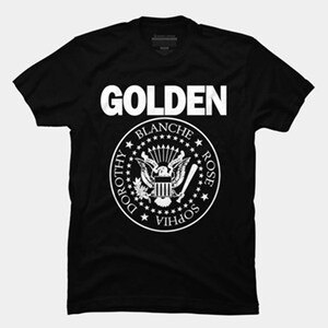 May include: Black t-shirt with a white graphic of the word "GOLDEN" above a stylized presidential seal with the names "DOROTHY, BLANCHE, ROSE, SOPHIA" around the perimeter.