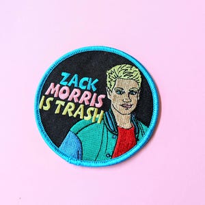 May include: Embroidered patch with a black background and a portrait of a person with blonde hair and blue eyes. The text "ZACK MORRIS IS TRASH" is in yellow, pink, and green. The patch has a blue border and is on a pink background.