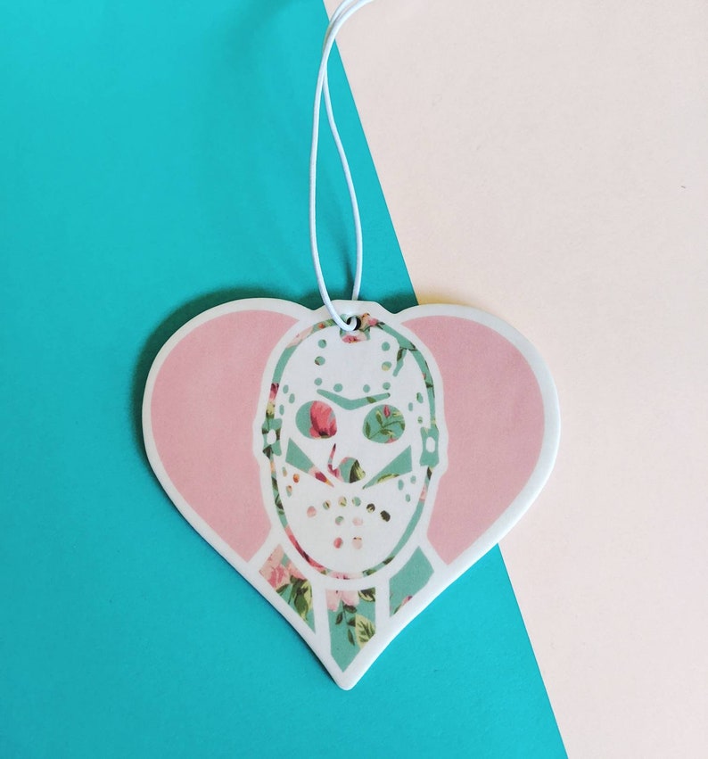 May include: A pink heart-shaped car air freshener with a white floral pattern and a white hockey mask with a floral pattern.