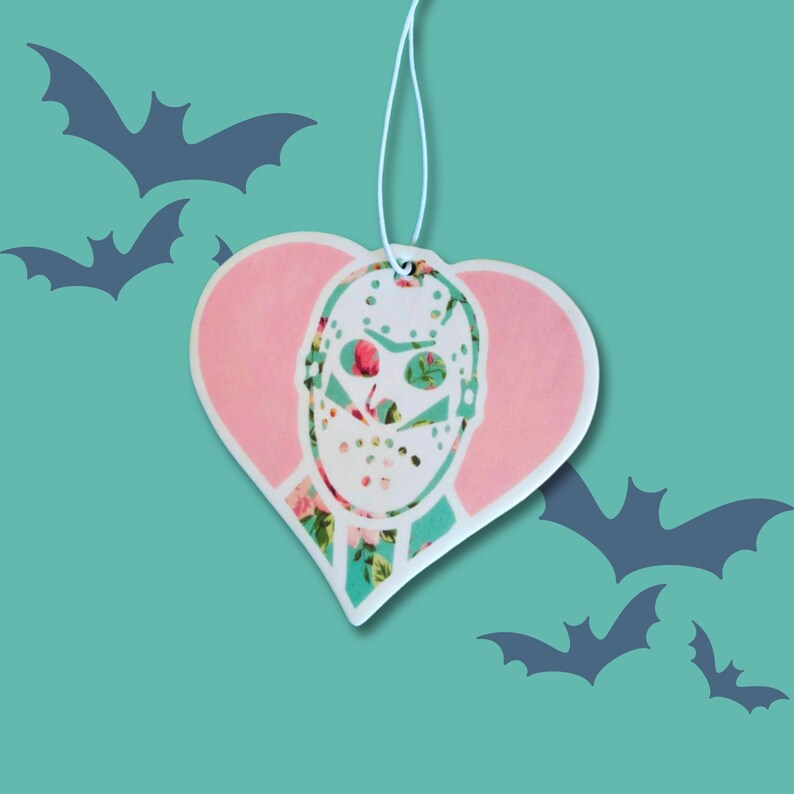 May include: A pink heart-shaped car air freshener with a white floral pattern and a white hockey mask with a floral pattern.