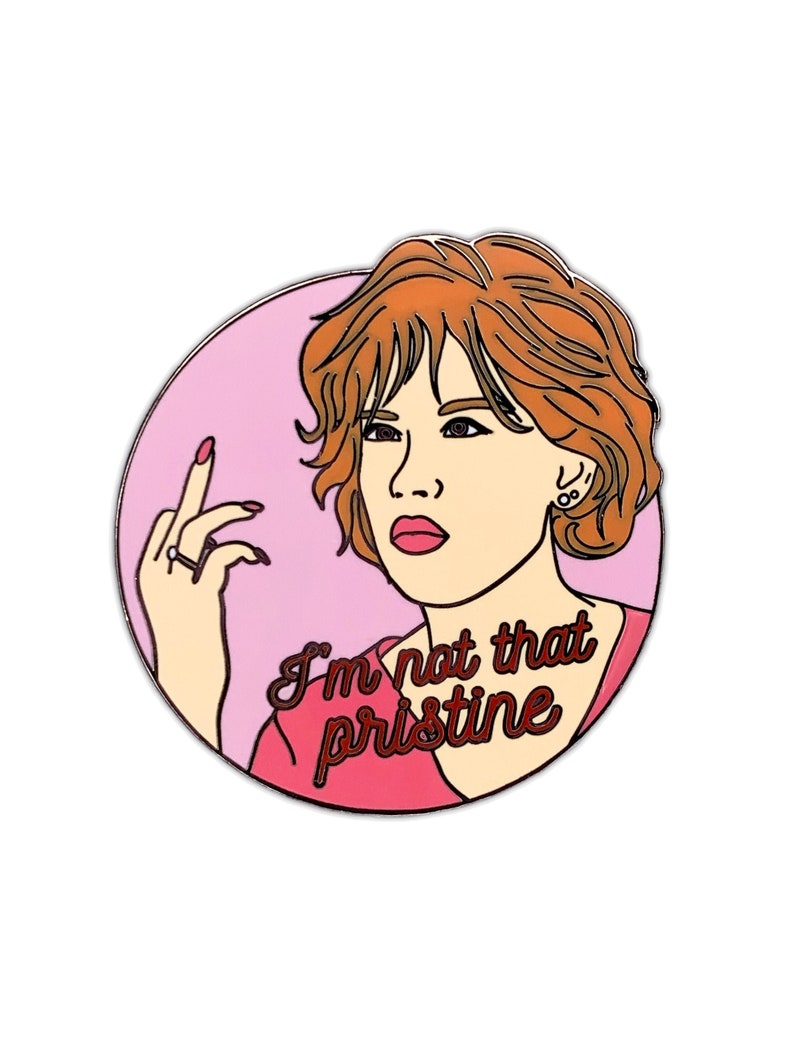 Puede incluir: Un pin de esmalte rosa y rojo con una mujer de dibujos animados de pelo rojo haciendo el dedo medio. El texto "I'm not that pristine" est&aacute; escrito en cursiva roja.