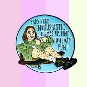 May include: A blue enamel pin featuring a cartoon illustration of a person sitting on a skateboard with the text "Two very enthusiastic thumbs up. Fine holiday fun!"