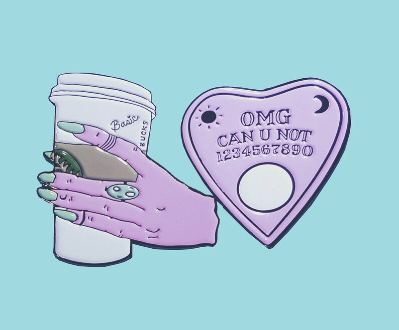 Op de afbeelding: Paarse emaille pinset met een koffiebeker met de tekst "Basic Bucks" en een paars hartvormig Ouija-bord met de tekst "OMG CAN U NOT 1234567890".