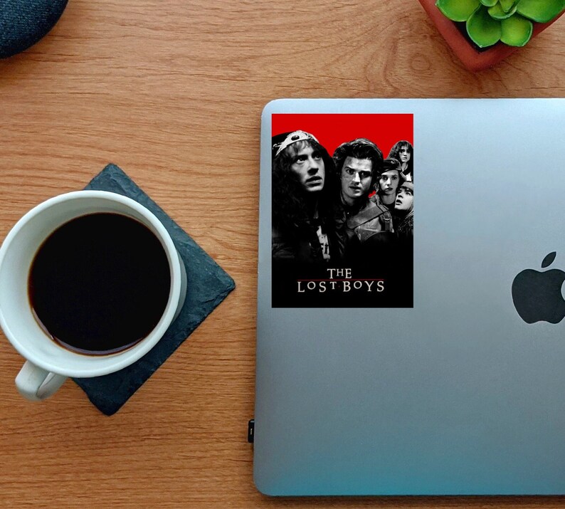 K&ouml;nnte beinhalten: Ein Schwarzwei&szlig;-Poster mit rotem Hintergrund, das eine Gruppe junger M&auml;nner zeigt. Das Poster zeigt den Text "The Lost Boys" in wei&szlig;.