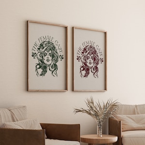 May include: Two framed prints with the text "The Female Gaze" and a stylized illustration of a woman with snakes for hair. The print on the left is green and the print on the right is maroon.