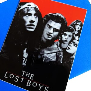 K&ouml;nnte beinhalten: Ein Schwarzwei&szlig;-Poster mit rotem Hintergrund, auf dem der Filmtitel "THE LOST BOYS" zu sehen ist. Das Poster zeigt f&uuml;nf Charaktere aus dem Film, darunter einen Vampir mit Lederjacke und eine Gruppe junger Leute.