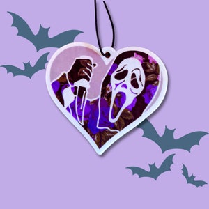 May include: A white heart-shaped car air freshener with a purple and black floral pattern. The image features a silhouette of a person wearing a ghost mask holding a knife.
