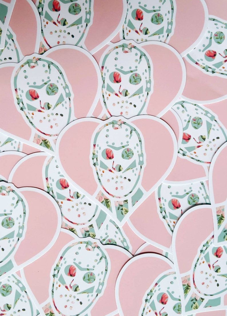 May include: A collection of pink heart-shaped stickers with a white hockey mask design. The masks are overlaid with a floral pattern in shades of green and pink.