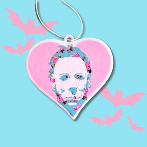 May include: A pink heart-shaped car air freshener with a floral pattern and a white silhouette of a man's face.