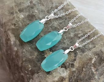 May include: Three silver necklaces with light blue gemstone pendants. The pendants are faceted and have a rectangular shape.