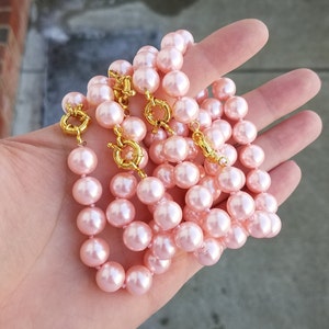 May include: A strand of pink faux pearl beads with gold clasps. The beads are strung on a thin, clear thread.