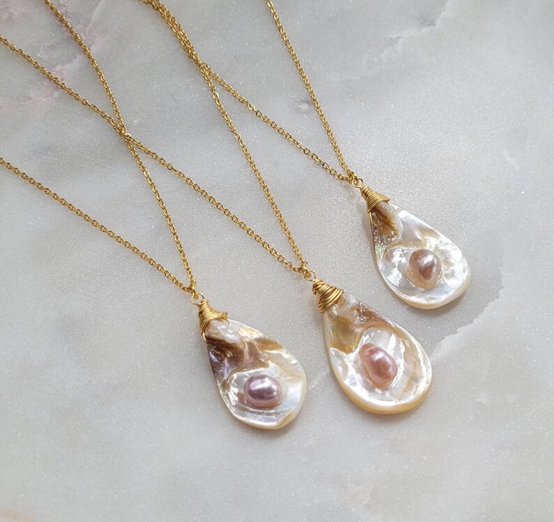 May include: Three gold necklaces with pearl and shell pendants. Each pendant is a different shape and size. The pearls are a light pink colour.