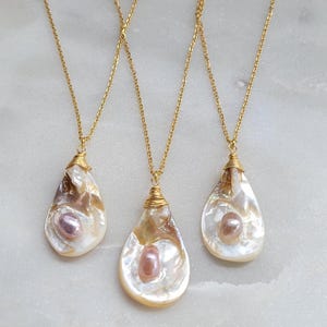 May include: Three gold chain necklaces with pearlescent shell pendants. Each pendant features a single pearl in the centre.