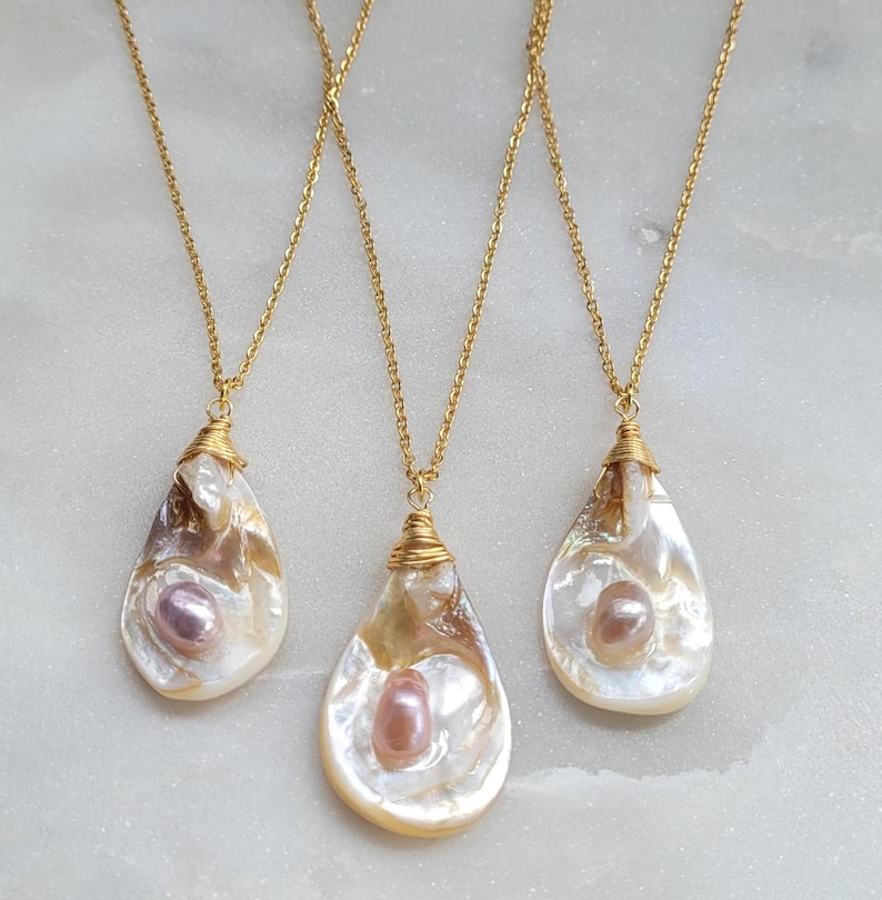 May include: Three gold chain necklaces with pearlescent shell pendants. Each pendant features a single pearl in the centre.