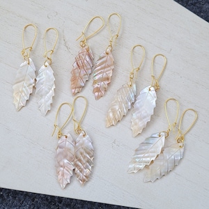 May include: Six pairs of gold leaf earrings with iridescent shell leaf charms. The earrings are all different sizes and shapes.