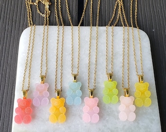 May include: Seven gold chains with gummy bear pendants in various pastel colors, including pink, blue, yellow, and green. The gummy bears are all in the shape of a standing bear.