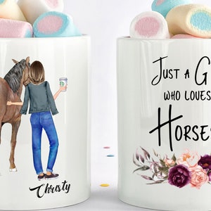 May include: Two white ceramic mugs with black text and images. The mug on the left has a brown horse and a woman holding a coffee cup. The text on the mug reads "Christy". The mug on the right has a floral design and the text "Just a girl who loves horses".