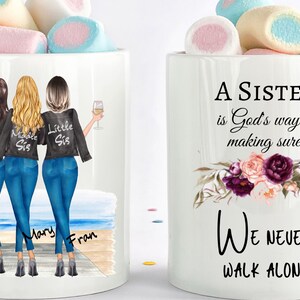 May include: White ceramic mug with a design of three sisters standing on a beach. The sisters are wearing jeans and jackets that say "Big Sis", "Middle Sis", and "Little Sis". The mug also has the text "A Sister is God's way of making sure We Never Walk Alone" with floral accents.