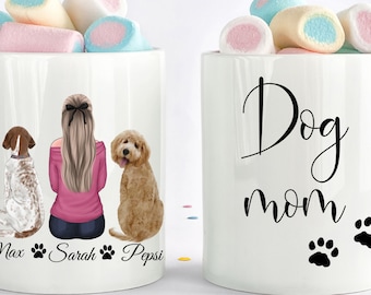 May include: White ceramic mug with a black illustration of a woman with blonde hair and two dogs. The text "Max, Sarah, Pepsi" is printed below the illustration. The other mug is white with the text "Dog mom" and two black paw prints.