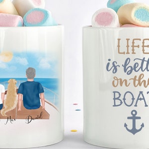 May include: A white ceramic mug featuring a colourful illustration of a couple and their dog on a boat. The text "Emily Max Daniel" is printed below the illustration. The other mug is white with the text "LIFE is better on the BOAT" and an anchor symbol.