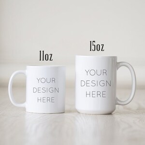 May include: Two white ceramic mugs with black text. The smaller mug is 11oz and the larger mug is 15oz. Both mugs say "Your Design Here".