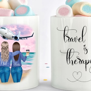 May include: Two white coffee mugs with a travel theme. One mug features a cartoon illustration of two women with suitcases and an airplane in the background. The other mug has the text "Travel is our therapy" with a heart and airplane design.