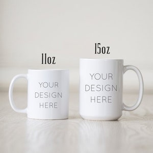 May include: Two white ceramic mugs with black text. The smaller mug is 11 oz and the larger mug is 15 oz. Both mugs say "Your Design Here".