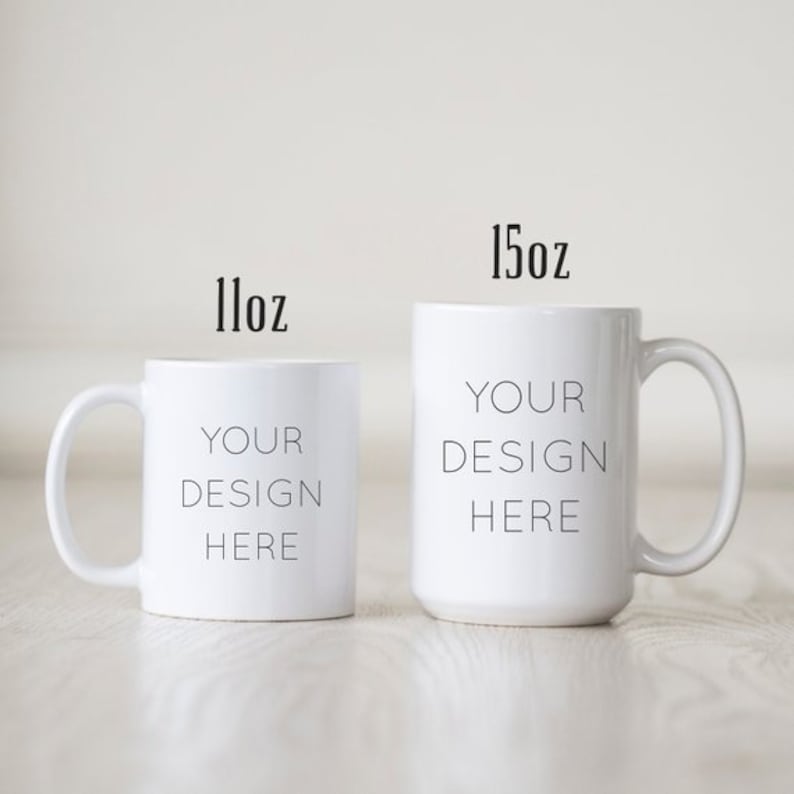 May include: Two white ceramic mugs with black text. The smaller mug is 11 oz and the larger mug is 15 oz. Both mugs say "Your Design Here".