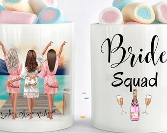 May include: White ceramic mugs with a design featuring three women in robes on a beach with the text "Bride Squad" and a bottle of champagne with two glasses on the other mug.