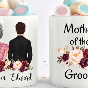 May include: Two white ceramic mugs filled with marshmallows. One mug features a couple illustration and the text "Mom Edward". The other mug says "Mother of the Groom" with floral accents.