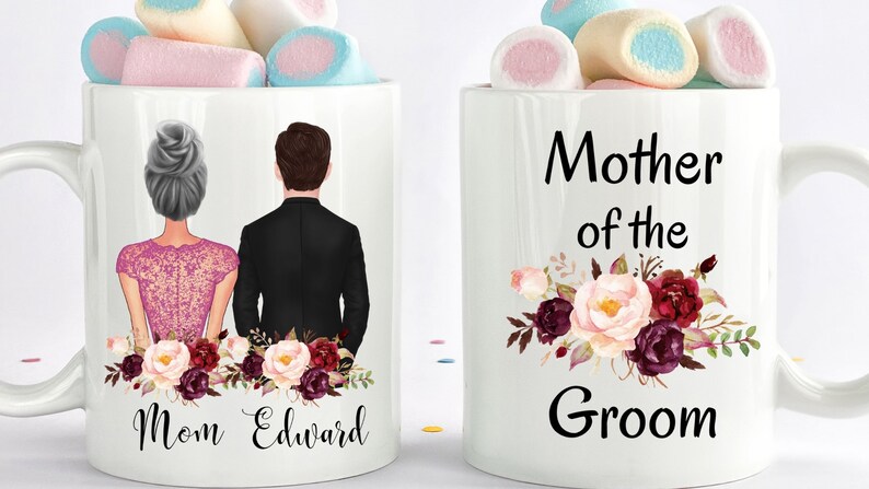 May include: Two white ceramic mugs filled with marshmallows. One mug features a couple illustration and the text "Mom Edward". The other mug says "Mother of the Groom" with floral accents.