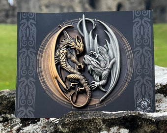 May include: A silver and gold dragon sculpture with intricate details. The dragons are facing each other in a battle pose. The sculpture is on a black background with a decorative border.