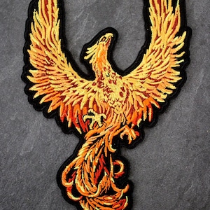 May include: Embroidered patch of a phoenix with wings spread wide. The bird is rendered in orange, yellow, and red hues, outlined with a black border. Suitable for sewing or ironing onto clothing or fabric items.