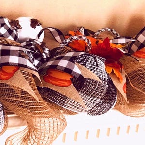 Puede incluir: Una guirnalda decorativa con calabazas naranjas, tela de cuadros negros y blancos y bucles de malla de arpillera de color tostado natural. El arreglo incluye hojas de oto&ntilde;o artificiales y el texto MemphisMomWreaths en la parte inferior izquierda.
