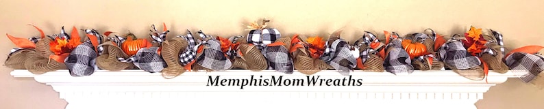 Puede incluir: Una guirnalda decorativa con calabazas naranjas, malla de arpillera marr&oacute;n y cinta de cuadros negros y blancos. La guirnalda est&aacute; adornada con hojas de oto&ntilde;o naranjas e incluye el texto MemphisMomWreaths centrado debajo del arreglo.