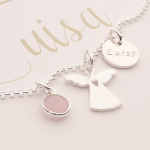 May include: Silver necklace with three charms: a pink stone, an angel with a heart cutout, and a round charm with the name "Luisa" engraved on it.