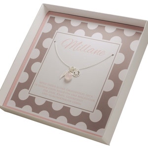 Puede incluir: Una caja de regalo blanca con un patr&oacute;n de lunares rosa y marr&oacute;n. La caja contiene un collar de plata con una piedra rosa y un dije que dice "Millane". El texto en la caja dice "Que esta peque&ntilde;a ala de &aacute;ngel te acompa&ntilde;e y proteja en tu vida. Te d&eacute; amor, fuerza, salud y confianza en ti mismo."