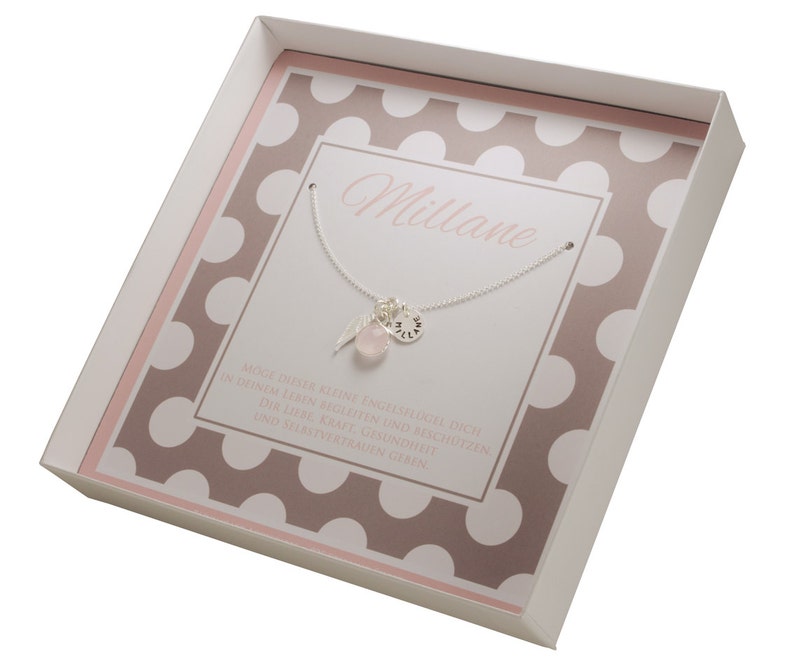 Puede incluir: Una caja de regalo blanca con un patr&oacute;n de lunares rosa y marr&oacute;n. La caja contiene un collar de plata con una piedra rosa y un dije que dice "Millane". El texto en la caja dice "Que esta peque&ntilde;a ala de &aacute;ngel te acompa&ntilde;e y proteja en tu vida. Te d&eacute; amor, fuerza, salud y confianza en ti mismo."