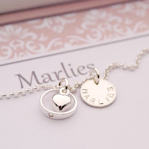Può includere: Collana d'argento con un ciondolo a forma di cuore e un ciondolo rotondo con il nome "Marlies" inciso.