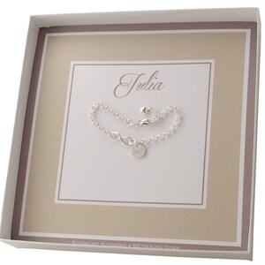 May include: A white gift box with a silver infinity bracelet inside. The bracelet has a small charm with the name "Julia" engraved on it. The box has a brown border and the text "Bloomingart Accessories - 925 Sterling Silver" printed on the bottom.