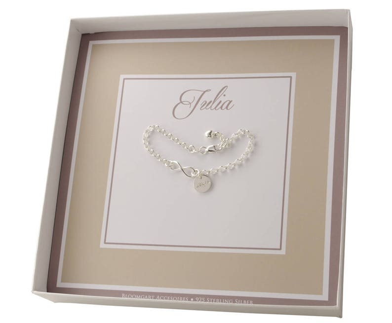 May include: A white gift box with a silver infinity bracelet inside. The bracelet has a small charm with the name "Julia" engraved on it. The box has a brown border and the text "Bloomingart Accessories - 925 Sterling Silver" printed on the bottom.
