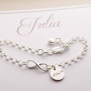 May include: Silver infinity charm bracelet with a personalized name tag that reads "Julia".